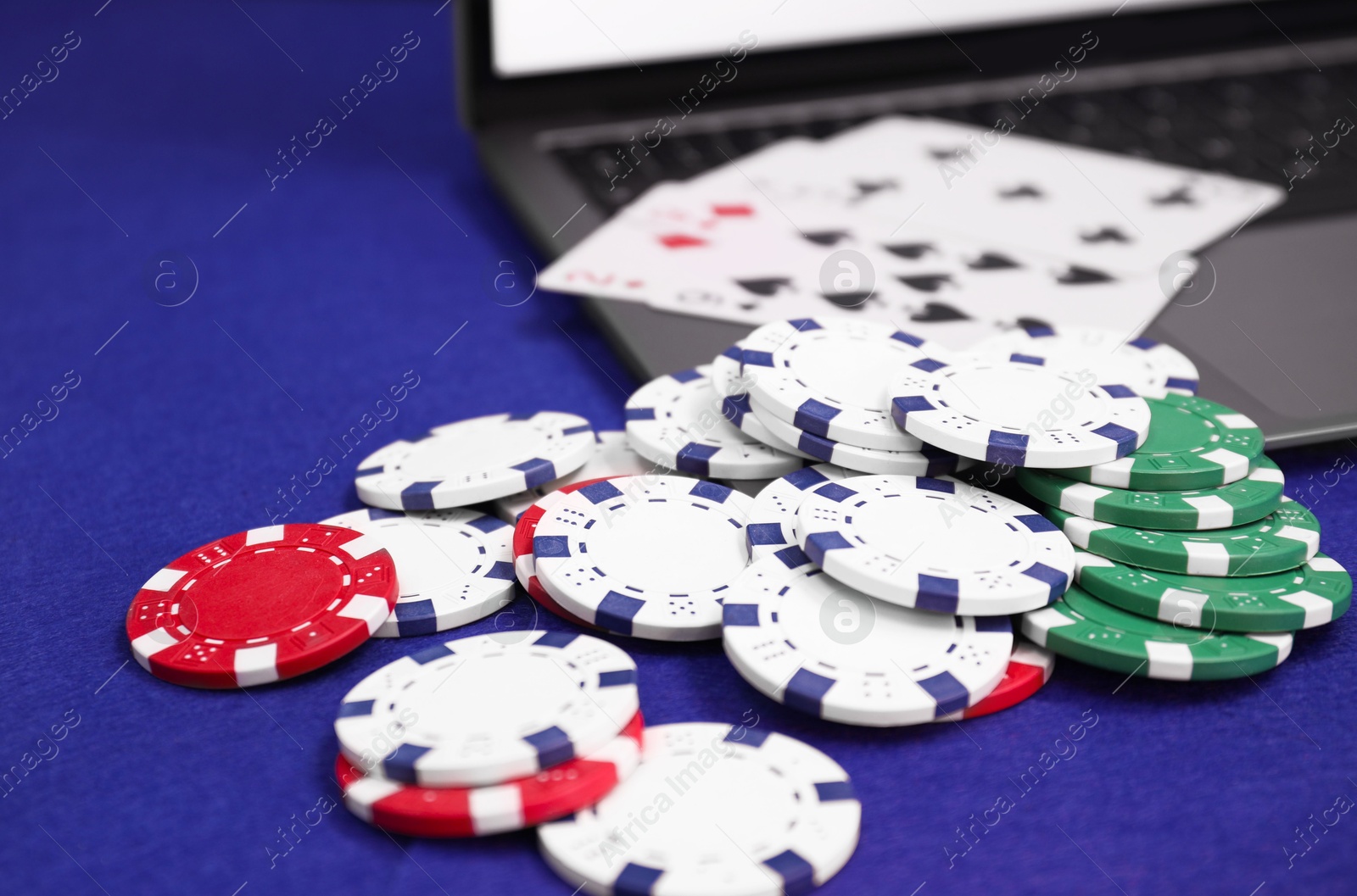 Photo of Laptop, poker chips and playing cards on blue table, closeup. Online game