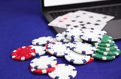 Photo of Laptop, poker chips and playing cards on blue table, closeup. Online game