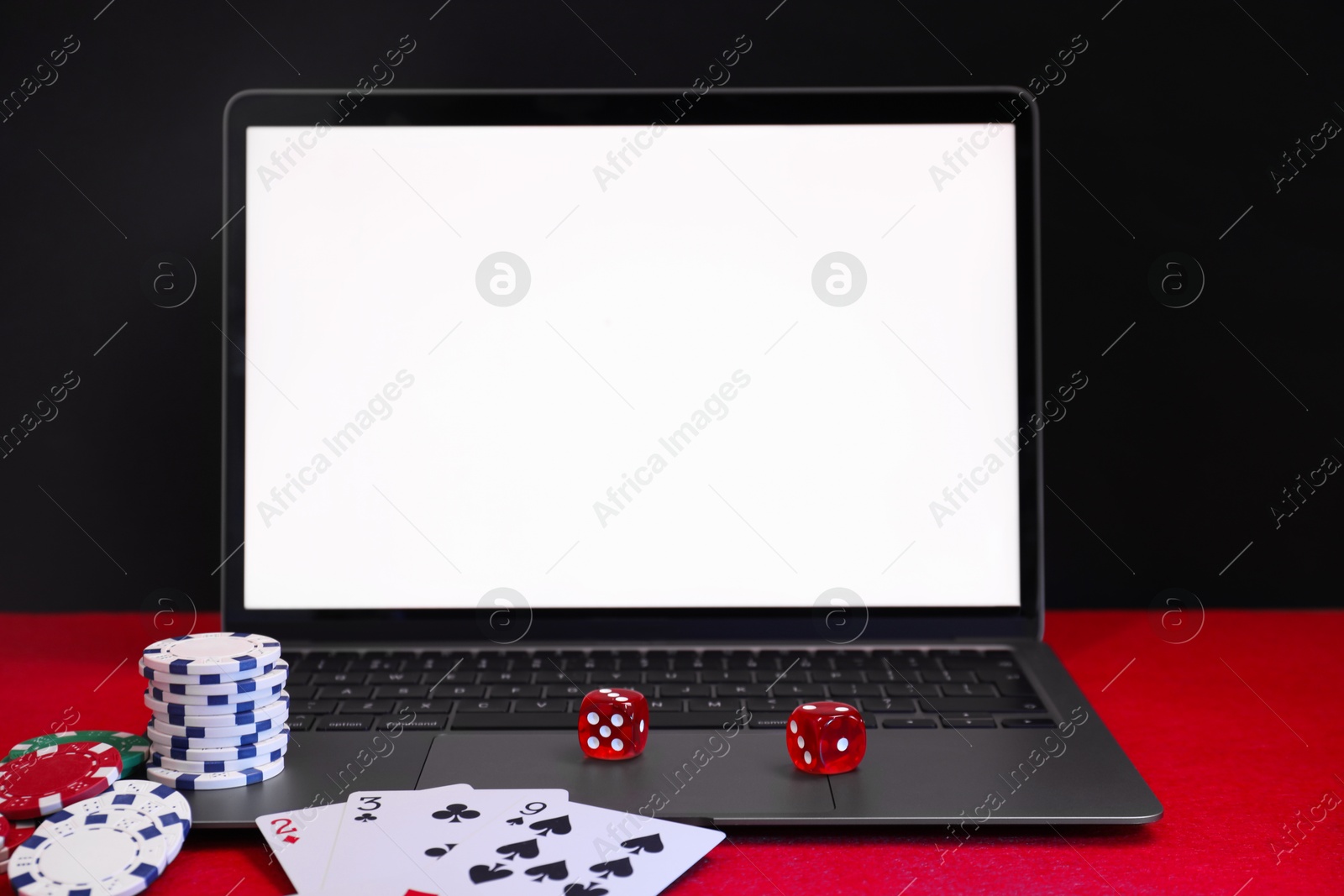 Photo of Laptop, poker chips, playing cards and dices on red table. Online game