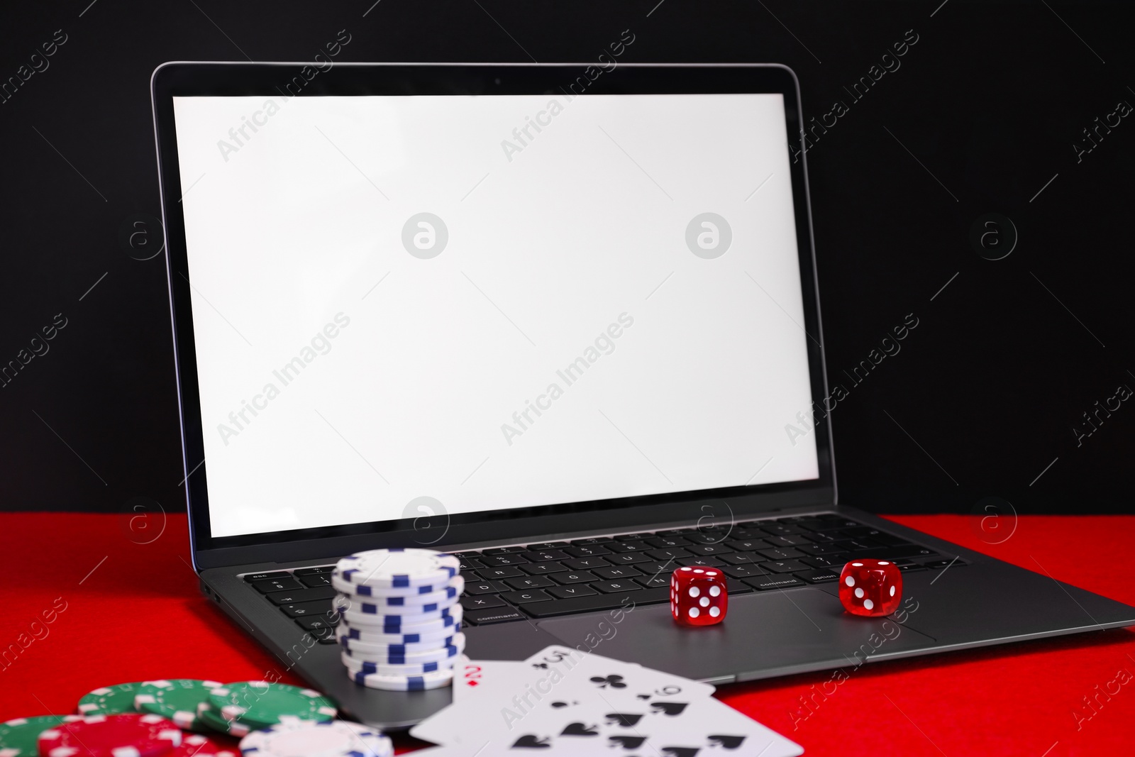 Photo of Laptop, poker chips, playing cards and dices on red table. Online game