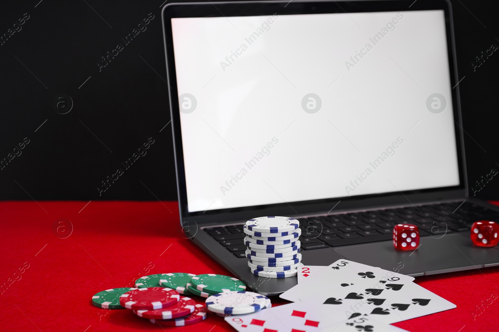 Photo of Laptop, poker chips, playing cards and dices on red table. Online game