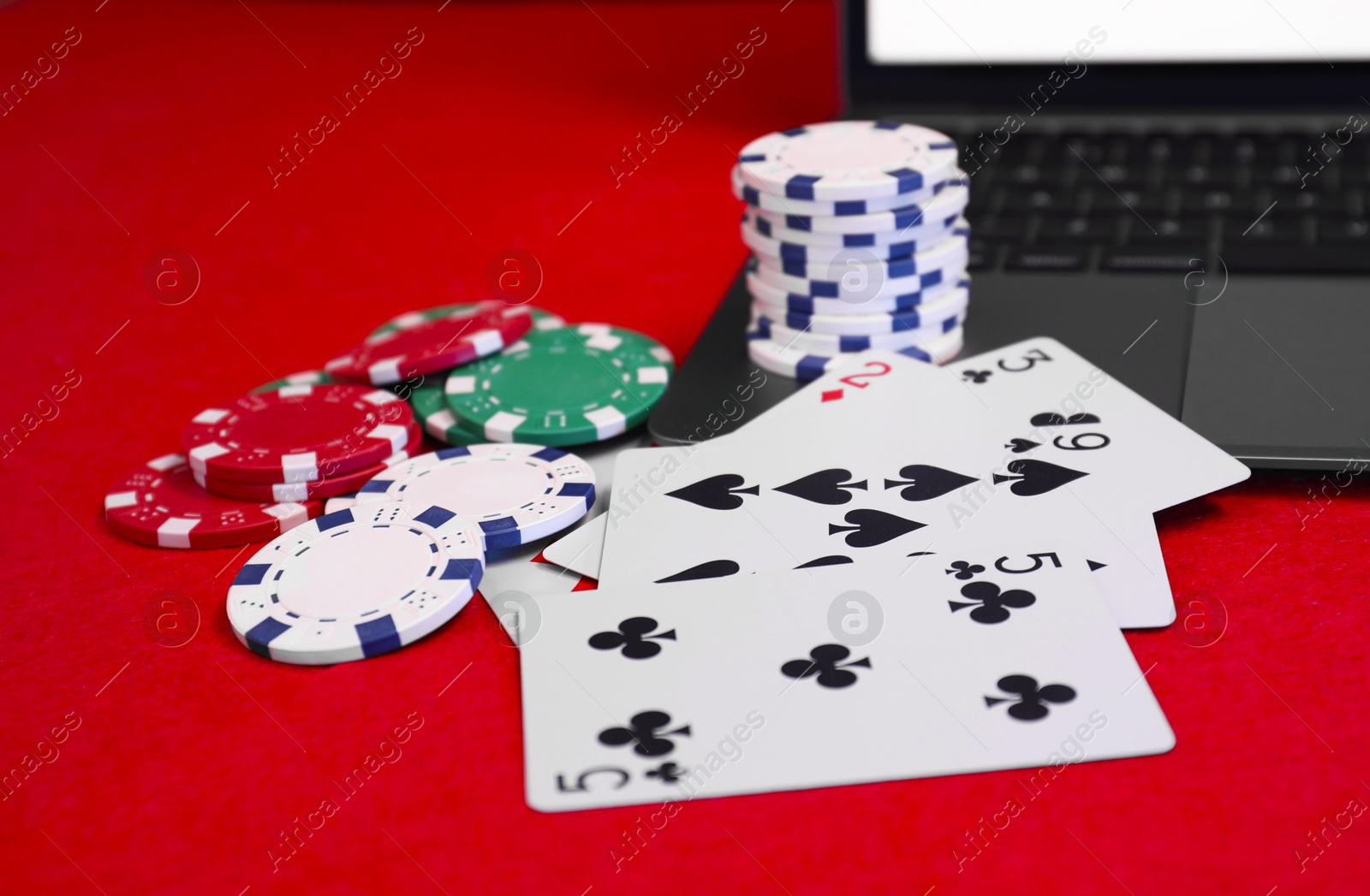 Photo of Laptop, poker chips and playing cards on red table, closeup. Online game