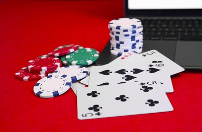 Photo of Laptop, poker chips and playing cards on red table, closeup. Online game