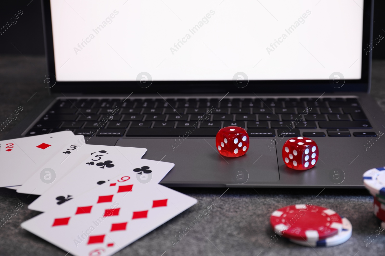 Photo of Laptop, poker chips, playing cards and dices on grey table, closeup. Online game