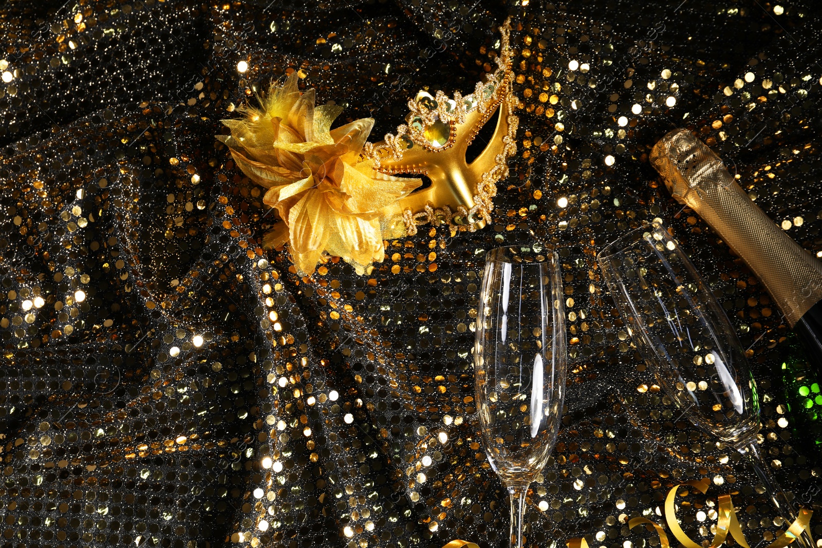 Photo of Beautiful carnival masks, champagne and glasses on fabric with golden sequins, flat lay