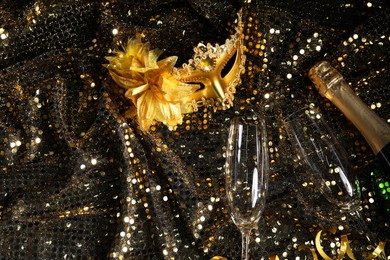 Beautiful carnival masks, champagne and glasses on fabric with golden sequins, flat lay