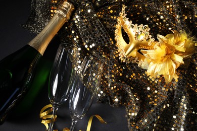 Beautiful carnival masks, champagne, glasses and fabric with golden sequins on black table, flat lay