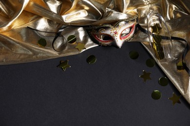 Photo of Beautiful carnival mask, champagne glass, confetti and silk fabric on black background, flat lay. Space for text