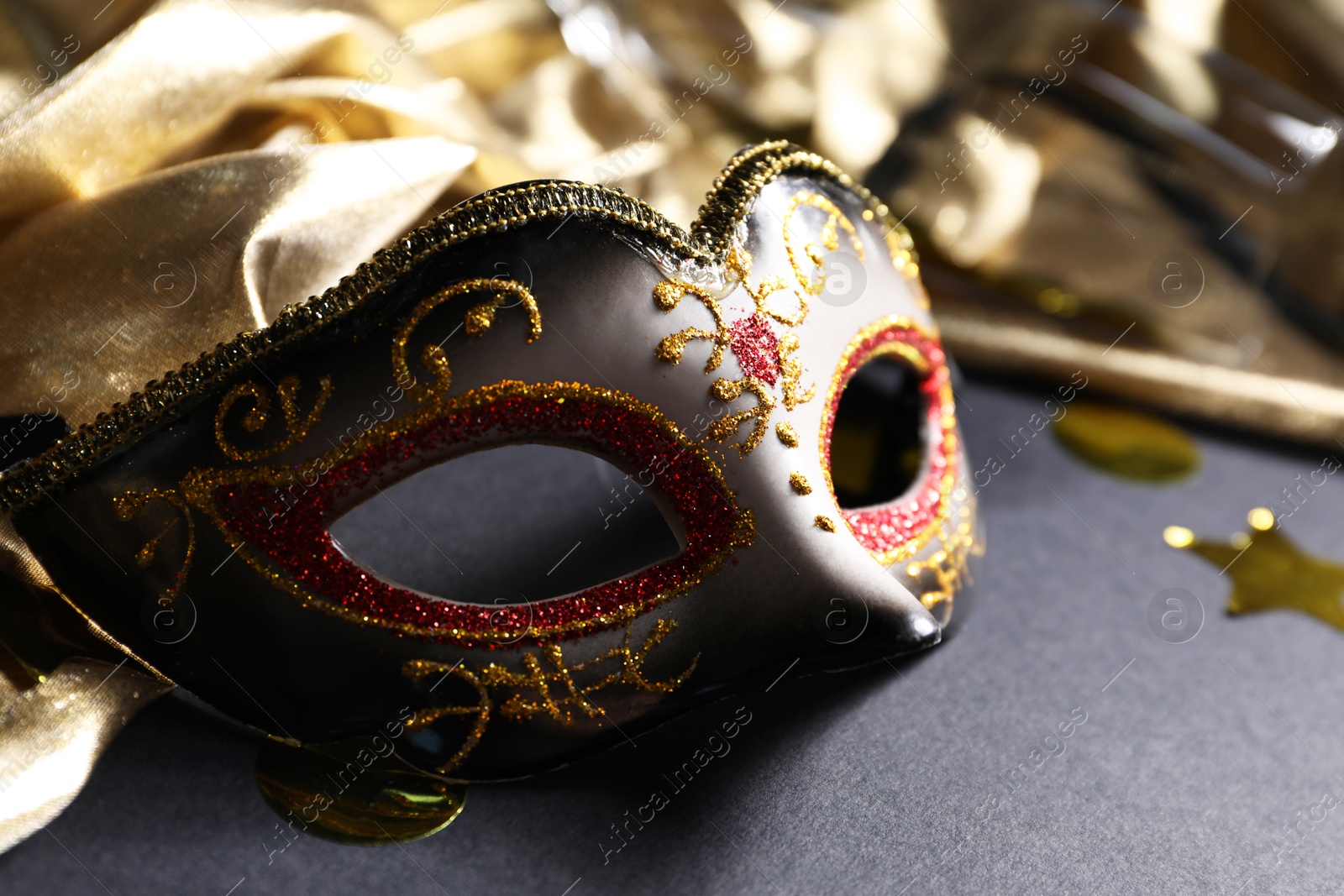 Photo of Beautiful carnival mask and silk fabric on black background, closeup