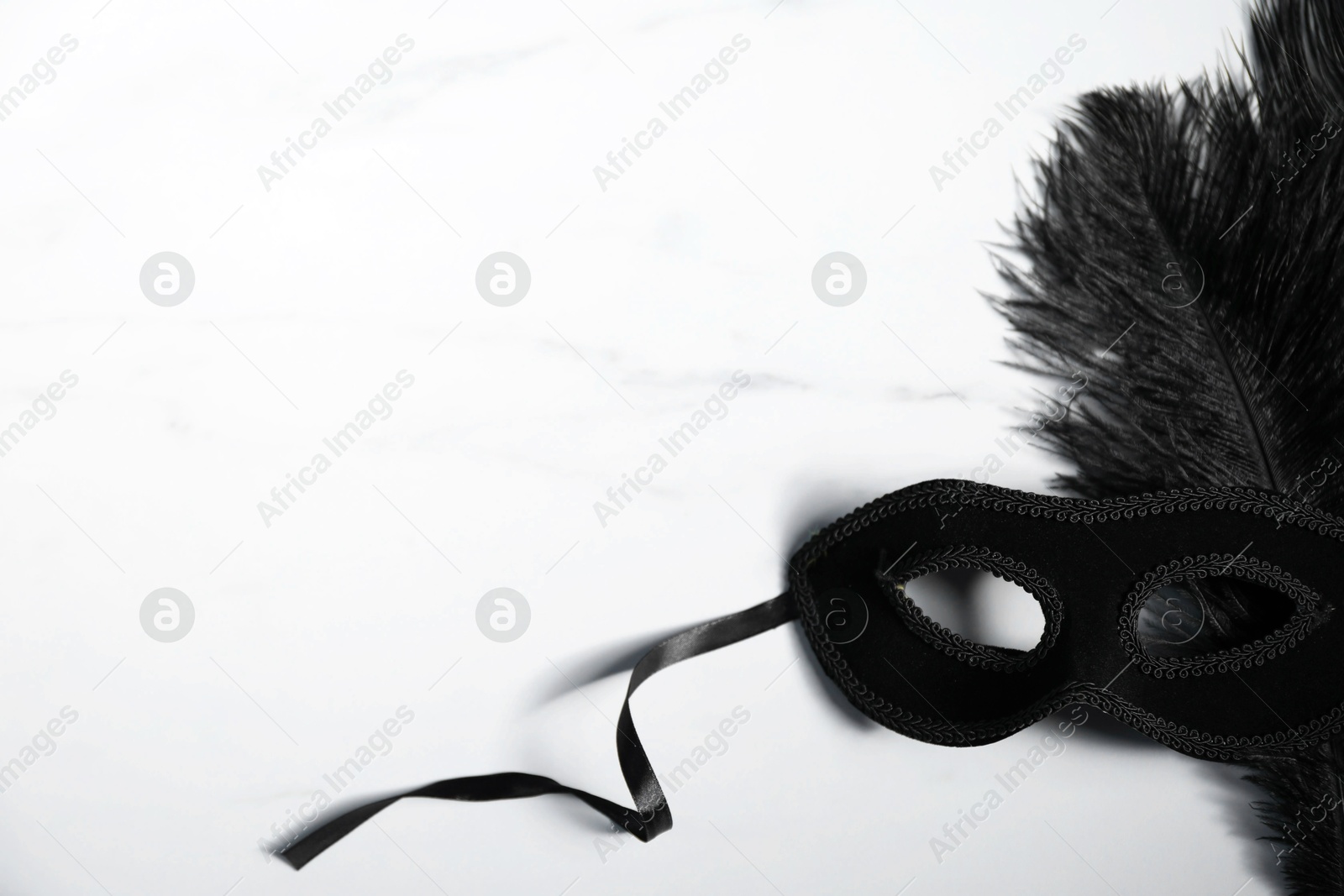 Photo of Beautiful black carnival mask on white marble table, space for text