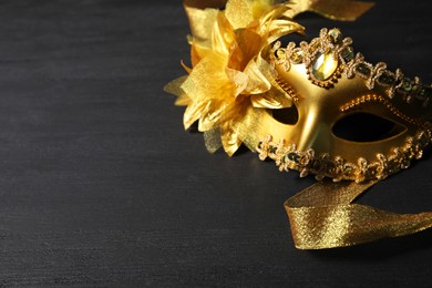 Photo of Beautiful golden carnival mask on black table, space for text