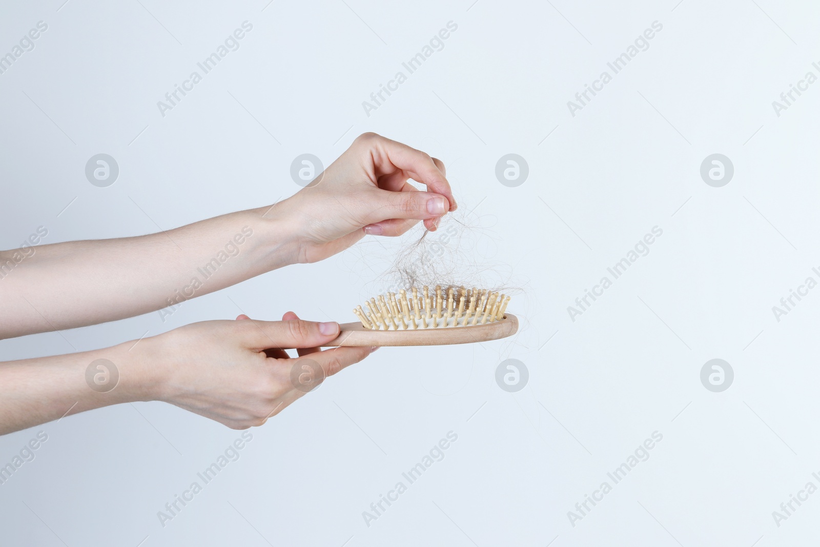 Photo of Woman taking lost hair from brush on light grey background, closeup. Space for text