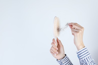 Woman taking lost hair from brush on light grey background, closeup. Space for text