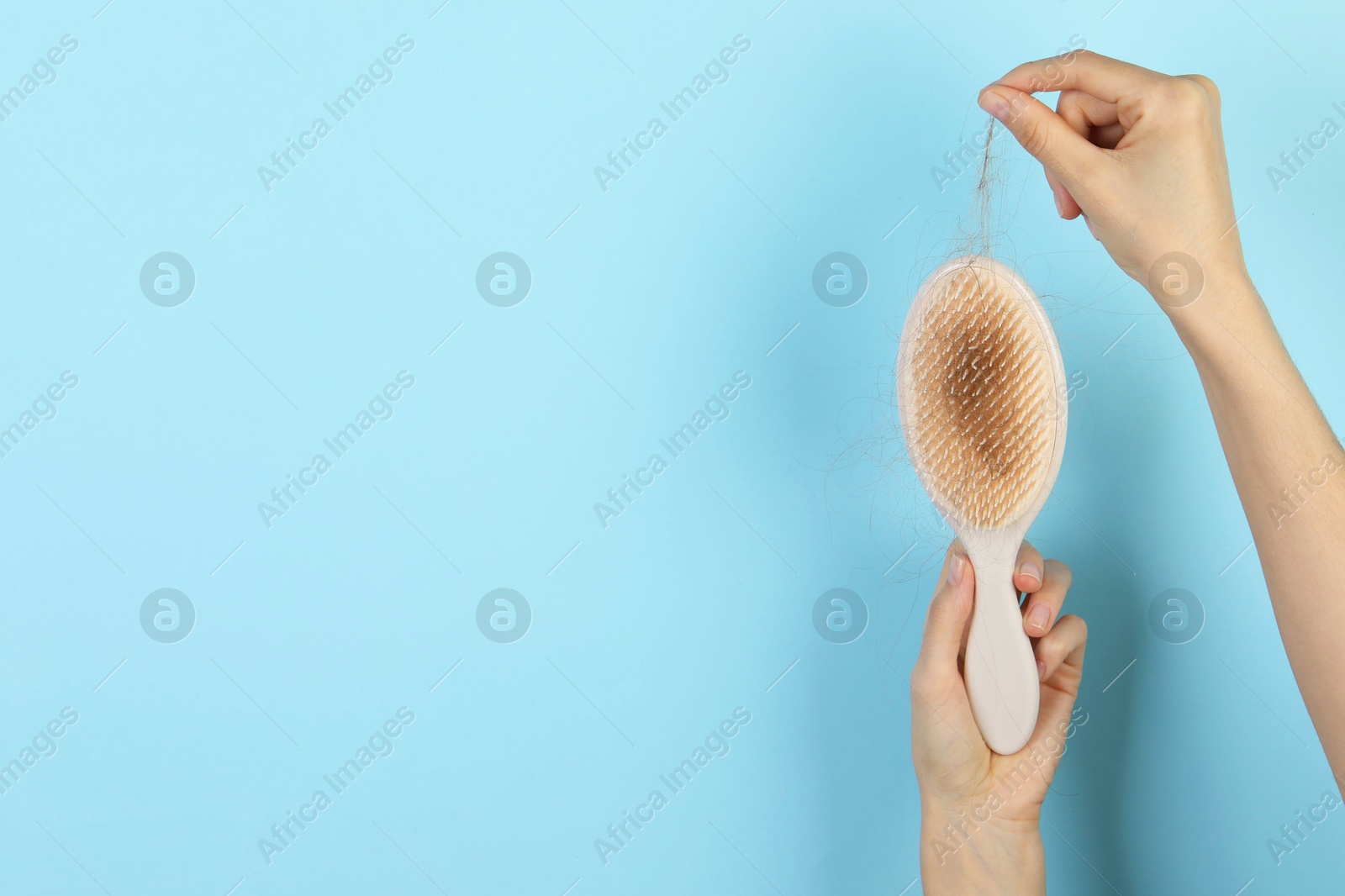 Photo of Woman taking lost hair from brush on light blue background, closeup. Space for text