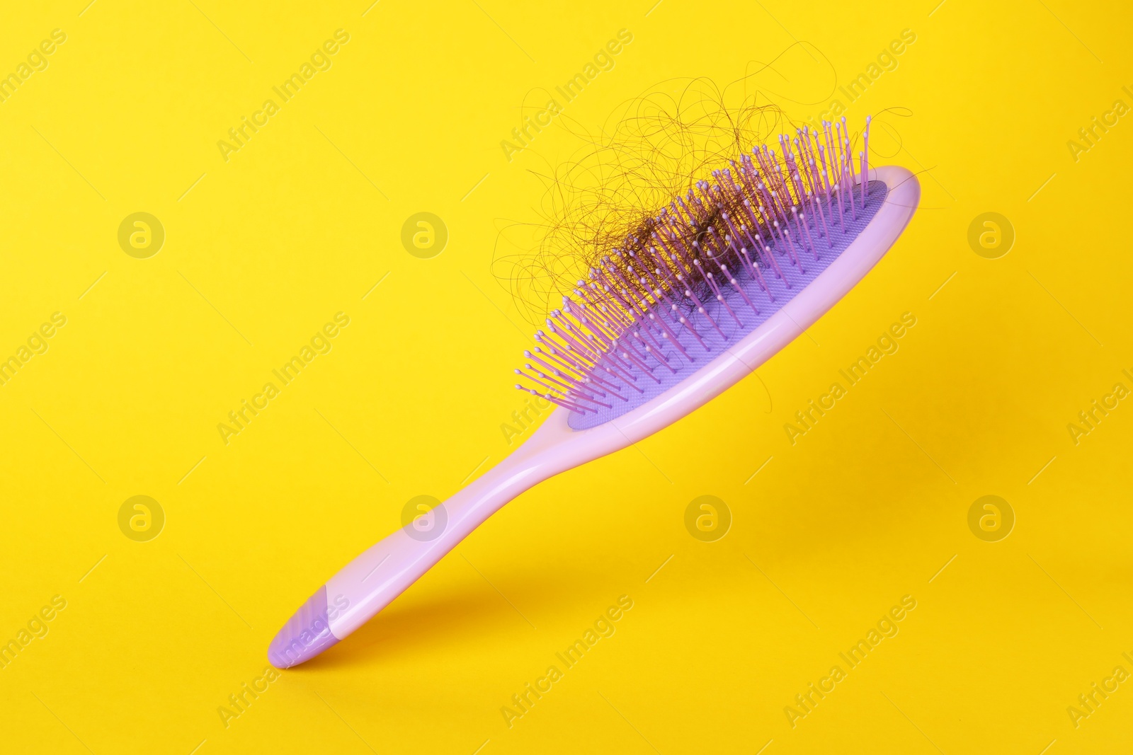 Photo of One brush with lost hair on yellow background, closeup