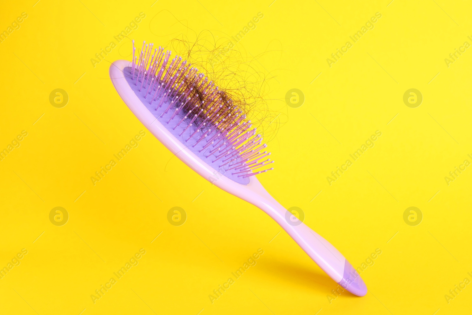 Photo of One brush with lost hair on yellow background, closeup