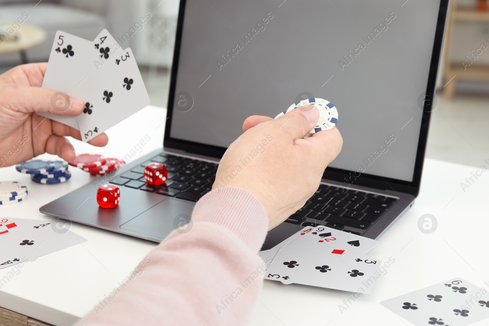 Photo of Online poker. Man holding playing cards and chip at white table with laptop, closeup