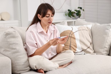 Photo of Worried young woman with pregnancy test on sofa at home