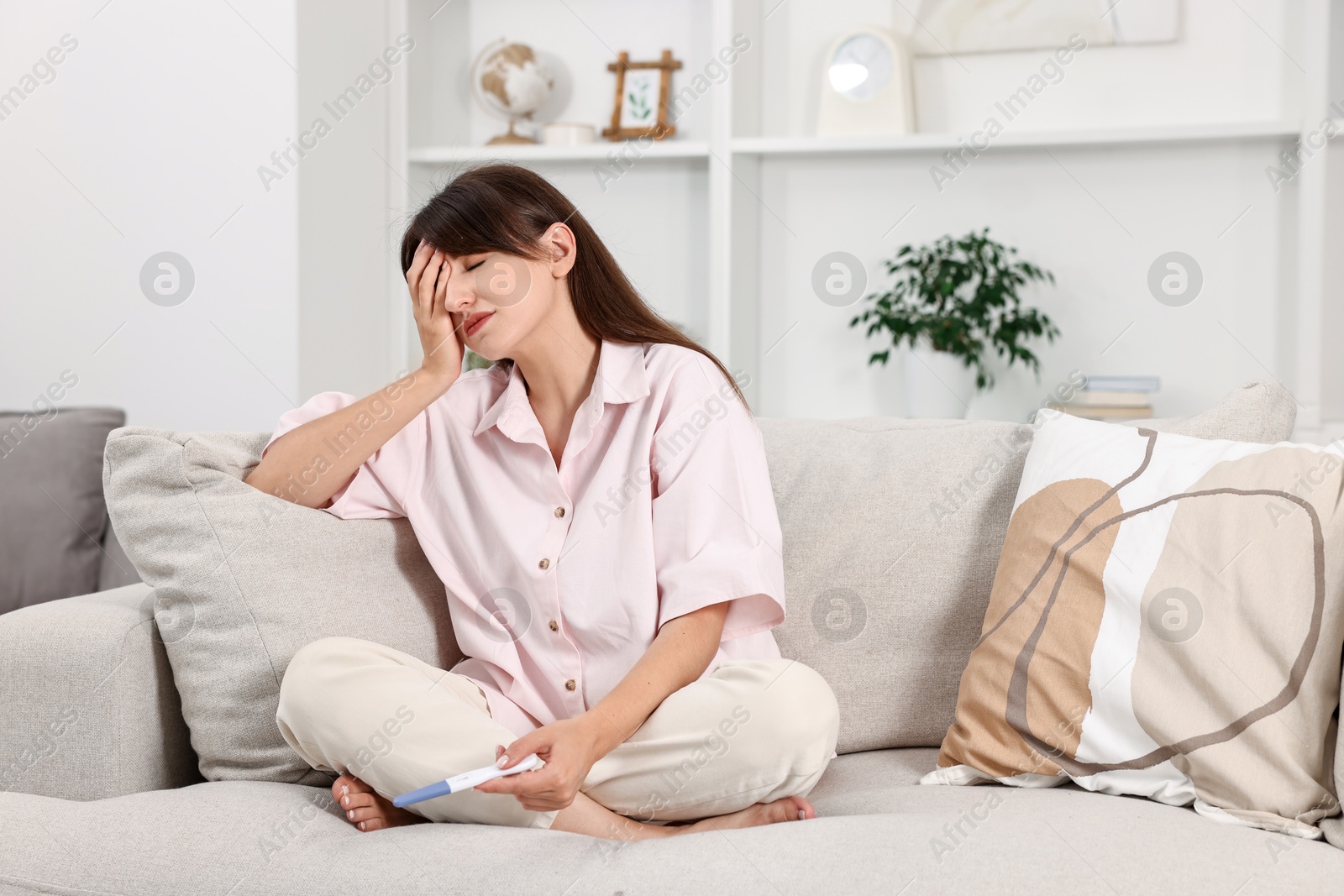 Photo of Worried young woman with pregnancy test on sofa at home