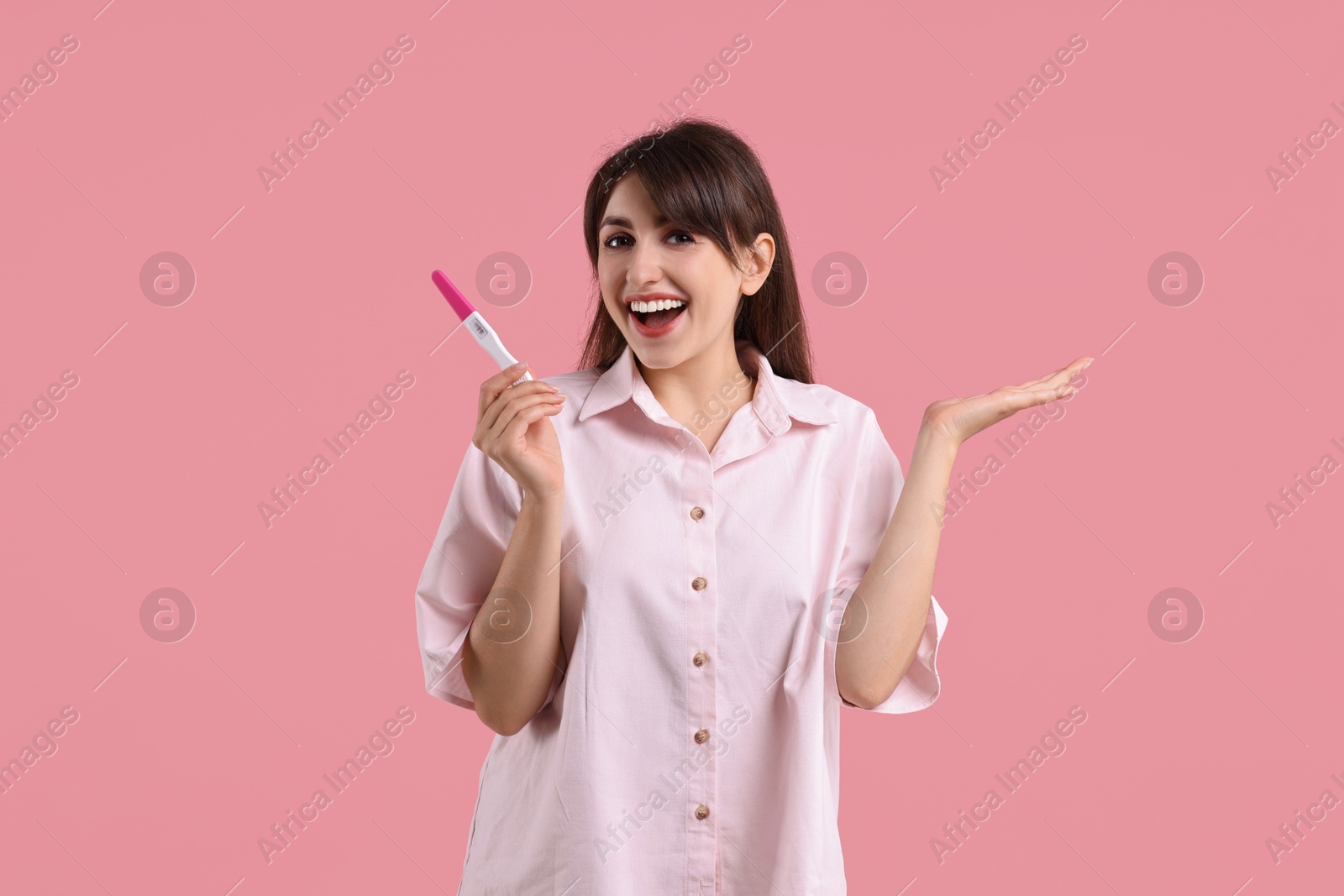 Photo of Happy young woman with pregnancy test on pink background