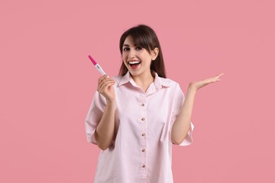 Happy young woman with pregnancy test on pink background