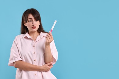 Worried young woman with pregnancy test on light blue background, space for text