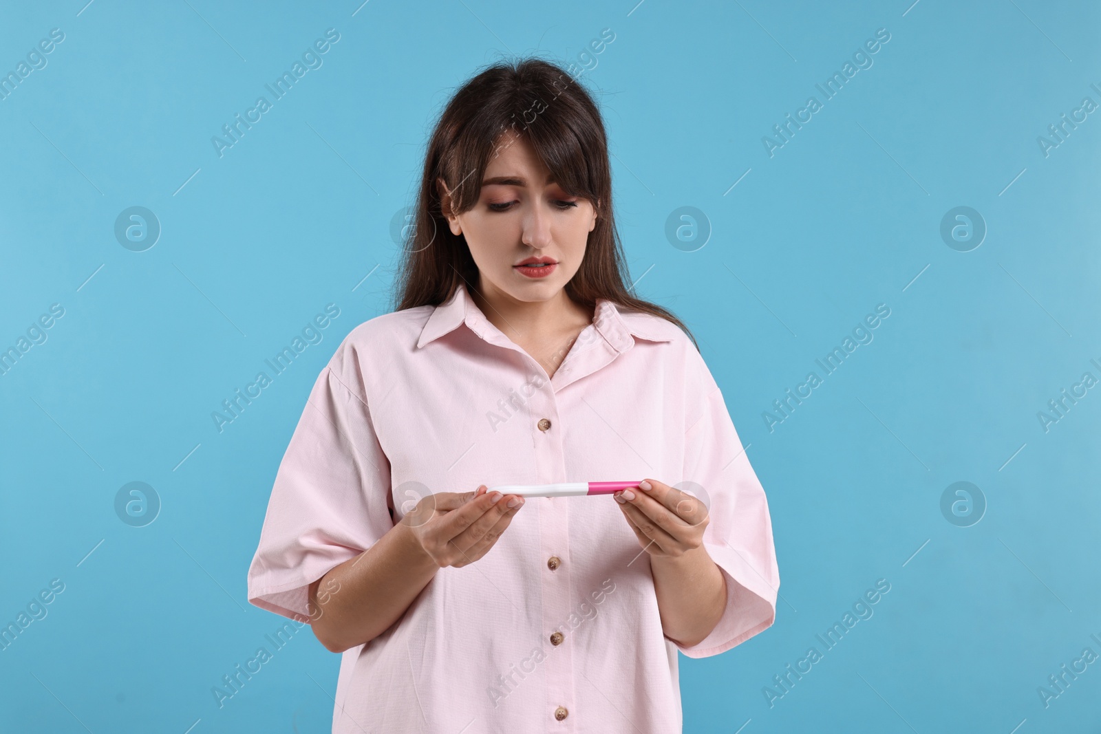 Photo of Worried young woman with pregnancy test on light blue background