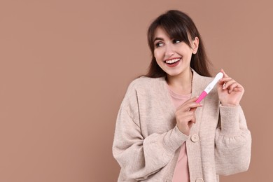 Happy young woman with pregnancy test on light brown background, space for text