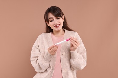 Photo of Happy young woman with pregnancy test on light brown background