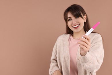 Photo of Happy young woman with pregnancy test on light brown background, selective focus. Space for text