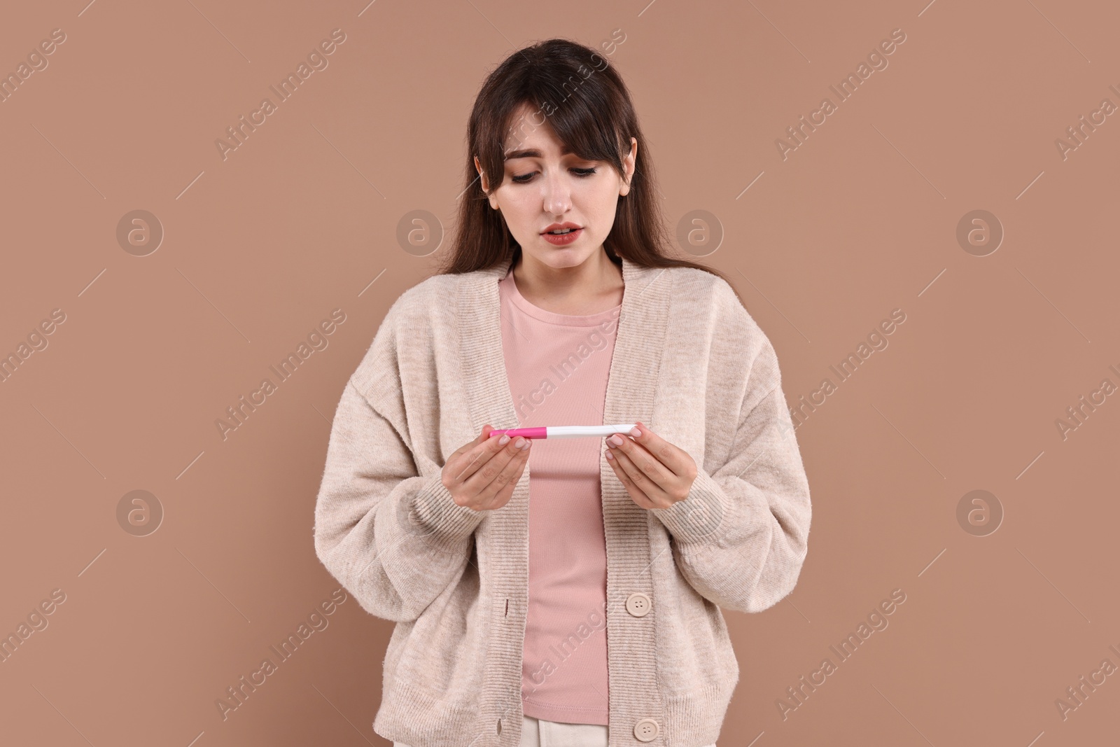 Photo of Worried young woman with pregnancy test on light brown background