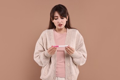 Photo of Worried young woman with pregnancy test on light brown background