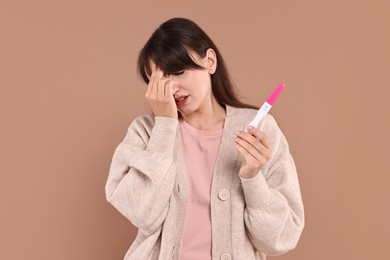 Worried young woman with pregnancy test on light brown background