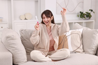 Photo of Happy young woman with pregnancy test on sofa at home