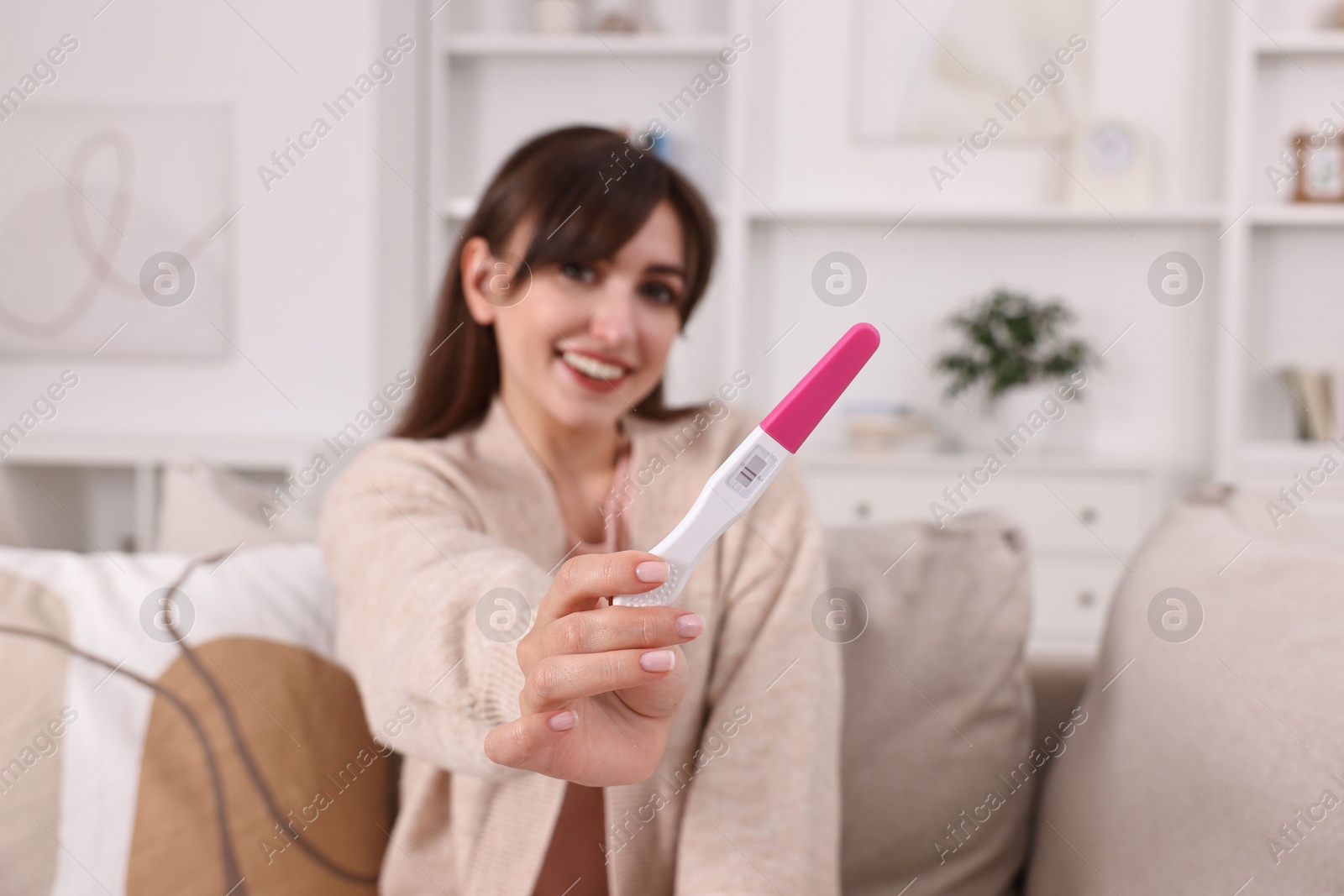 Photo of Happy young woman with pregnancy test on sofa at home