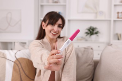 Happy young woman with pregnancy test on sofa at home