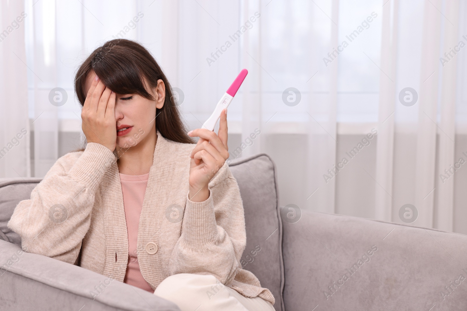 Photo of Worried young woman with pregnancy test on sofa at home