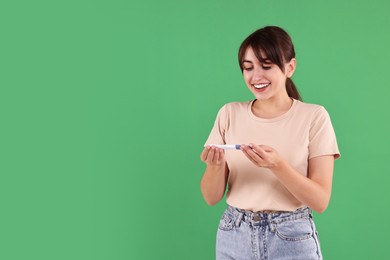 Happy young woman with pregnancy test on green background, space for text