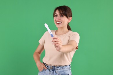 Photo of Happy young woman with pregnancy test on green background