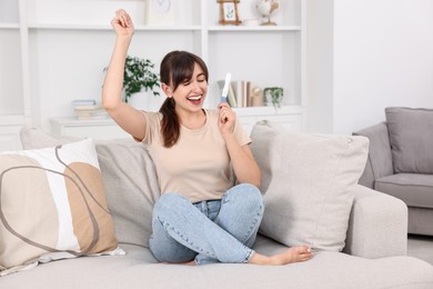 Photo of Happy young woman with pregnancy test on sofa at home