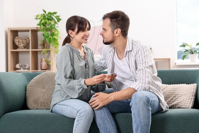 Happy young couple with pregnancy test on sofa at home