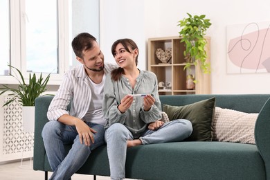 Happy young couple with pregnancy test on sofa at home