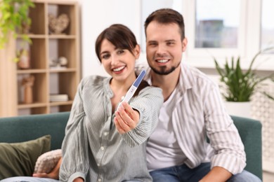 Photo of Happy young couple with pregnancy test on sofa at home, selective focus