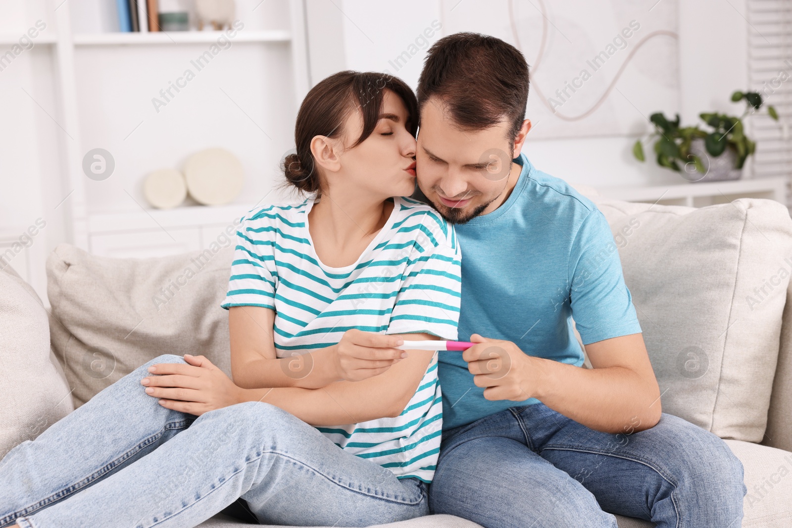 Photo of Happy young couple with pregnancy test on sofa at home