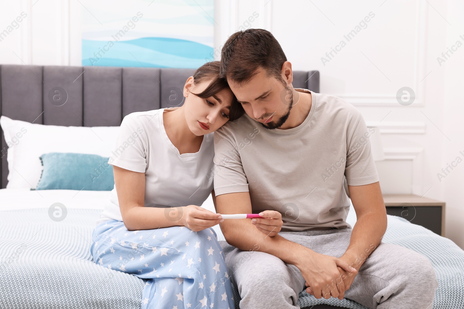 Photo of Worried young couple with pregnancy test on bed at home