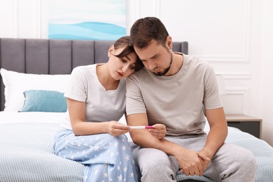 Photo of Worried young couple with pregnancy test on bed at home