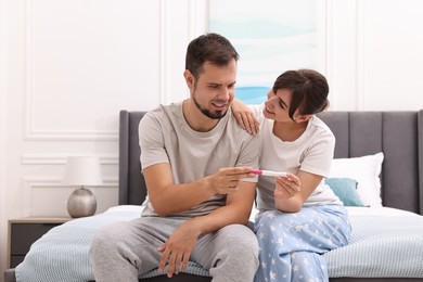 Happy young couple with pregnancy test on bed at home