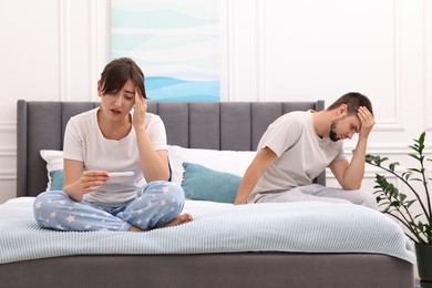 Photo of Worried young couple with pregnancy test on bed at home