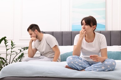 Worried young couple with pregnancy test on bed at home