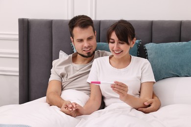 Happy young couple with pregnancy test on bed at home